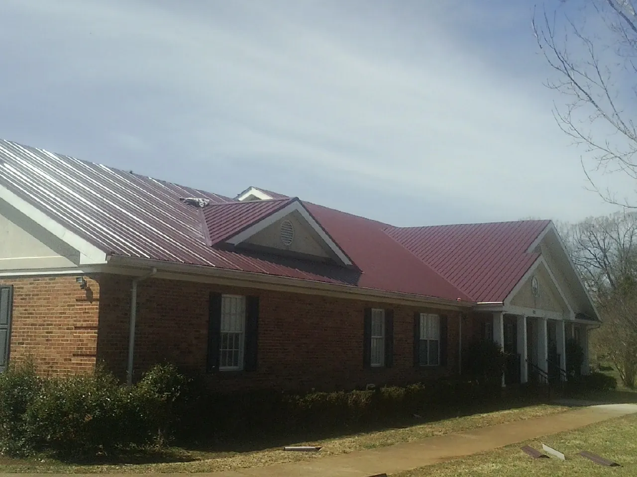 Red metal roof with gabled entries on a long brick building, from a Hail Damage Roof Repair job in Green Pond