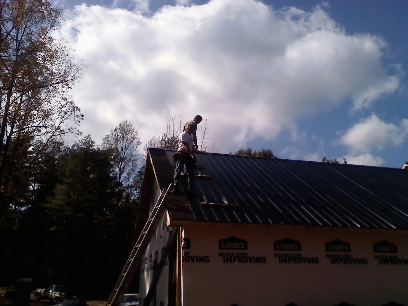 Roofer fastening dark metal panels high against a cloudy sky, from a Roof Inspection job in Green Pond