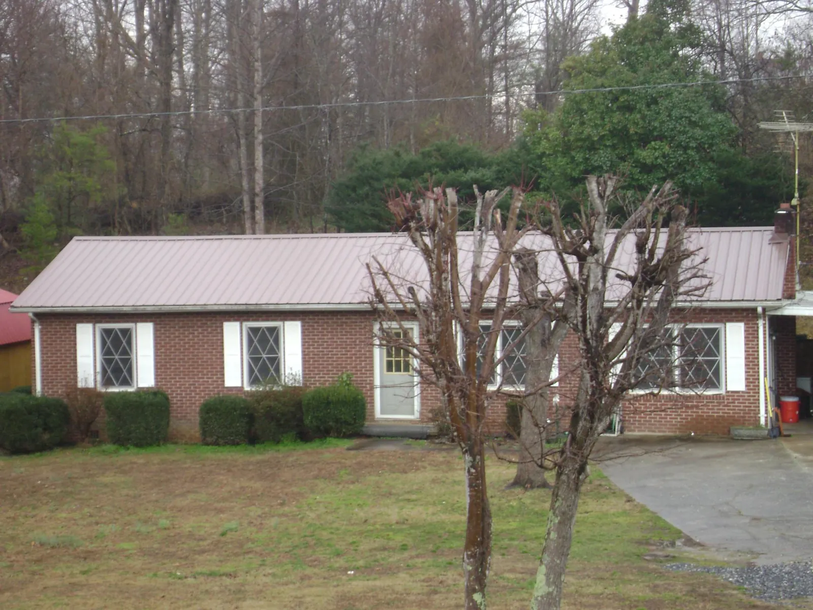 Mauve metal roof on a brick ranch home behind bare trees in Green Pond