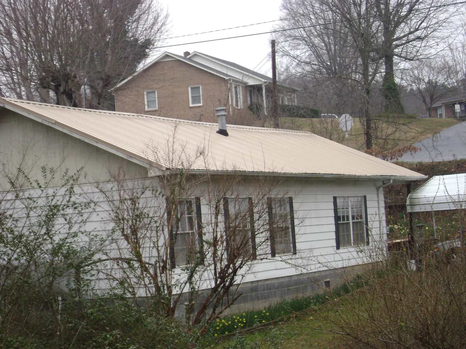 Tan metal roof on a white sided house set into a hillside — Commercial Roofing by Roofing Brothers in Green Pond